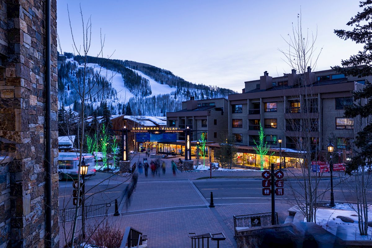 A picturesque winter scene with a ski resort, including buildings, trees with lights, and a snow-covered mountain in the background.