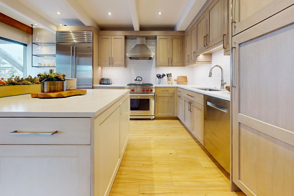 A modern kitchen with light wood cabinetry, a kitchen island, stainless steel appliances, and a window providing natural light ends the sentence.