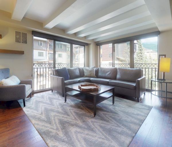 A modern living room with a large sectional sofa, armchair, coffee table, floor lamps, and a chevron-patterned rug, featuring large windows.