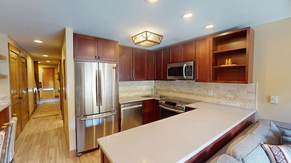 A modern U-shaped kitchen with stainless steel fridge, microwave, and range, dark wood cabinets, light countertop, tiled backsplash, and a cozy seating area.
