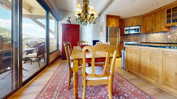 A kitchen with wooden cabinets, a dining table, and a chandelier, overlooking a balcony with a grill outside the sliding glass door.