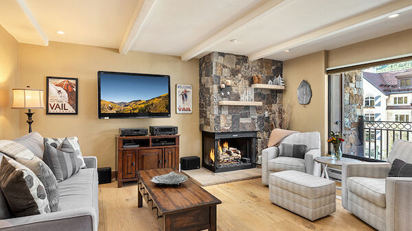 The image shows a cozy living room with a fireplace, TV, seating, and decorative elements, creating a welcoming atmosphere.