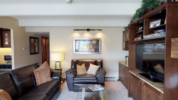 Cozy living room with brown leather sofa set, glass coffee table, built-in wood cabinet TV unit, framed art, and warm lighting. ending sentence.
