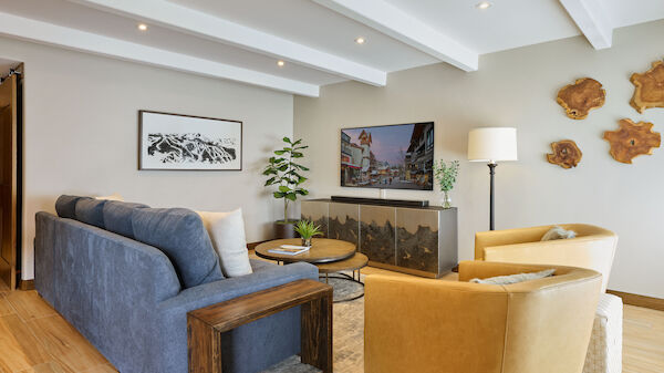 A modern living room with a blue sofa, two beige chairs, a TV, plants, a floor lamp, and wall art on wood flooring.