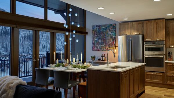 Modern open-concept kitchen and dining area with a central island, wooden cabinets, stainless steel appliances, a large windowed wall, and a dining table set for a meal.