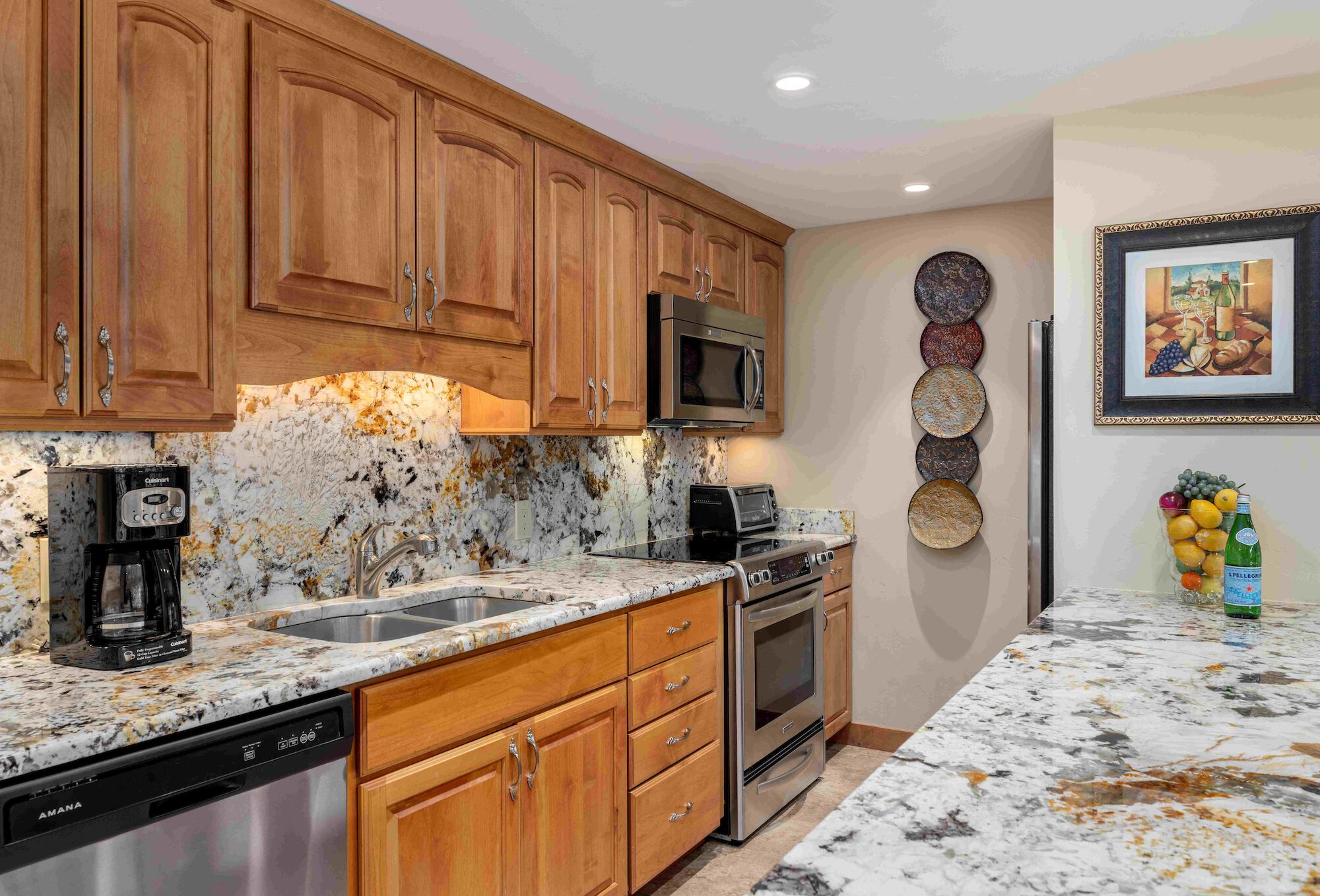 A modern kitchen with wooden cabinets, granite countertops, stainless steel appliances, a coffee maker, and a bright, airy layout.