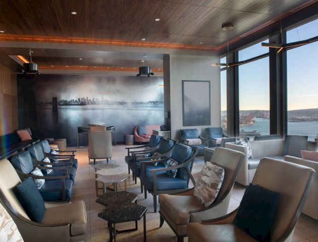 A modern lounge with ample seating, large windows showcasing a scenic view, and a mural of a city skyline on the back wall.