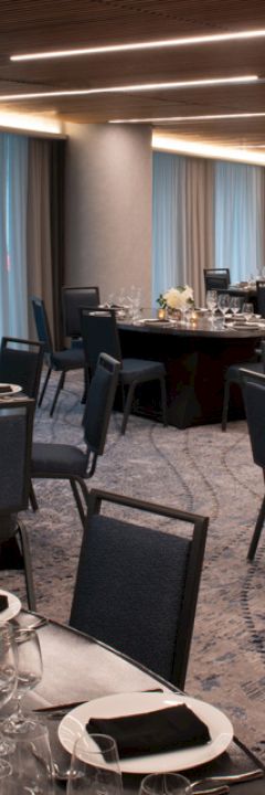 The image shows an elegant banquet hall set up with round tables, chairs, and neatly arranged table settings, featuring candles and flower centerpieces.