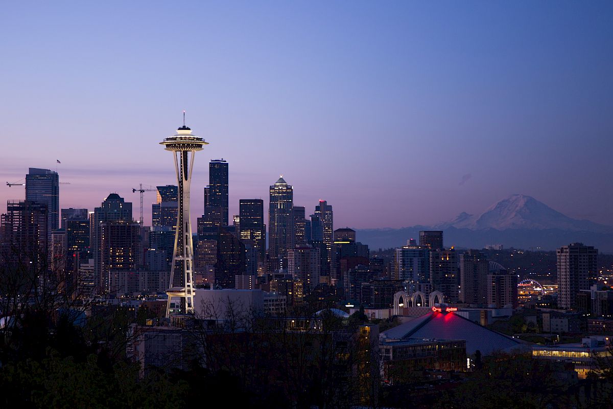 This image shows the Seattle skyline at dusk, featuring the Space Needle with Mount Rainier in the background, under a clear sky.