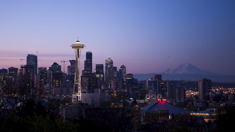 This image shows the Seattle skyline at dusk, featuring the Space Needle with Mount Rainier in the background, under a clear sky.